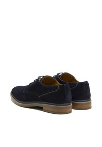 Chaussures en suède bleu marine avec une texture lisse, un bout arrondi et des accents au talon arrière. Présente des détails cousus et une semelle en caoutchouc marron.