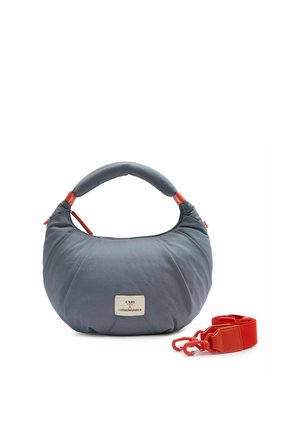 Sac à main bleu doux en forme de croissant avec une poignée rembourrée et une bandoulière rouge vif amovible, avec une petite étiquette de marque blanche à l'avant.