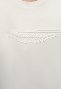 Λευκό πουκάμισο με ανάγλυφο λογότυπο Aston Martin με στυλιζαρισμένα φτερά και το όνομα της μάρκας στο κέντρο του στήθους.