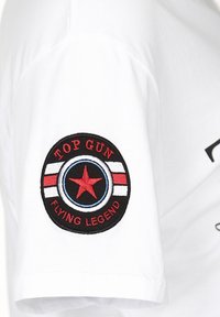 Witte katoen T-shirt met een zwart rond patch met rode en witte strepen, een blauwe cirkel, een rode ster en de tekst "TOP GUN FLYING LEGEND."