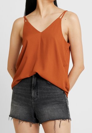 Camisole couleur rouille avec un décolleté en V, des bretelles fines et une coupe ample. Associée à un short en denim noir effiloché, créant un look superposé.
