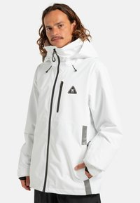 Witte waterdichte jas met een capuchon, ritssluiting en zwarte accenten. Bevat een borstzak en gestructureerde zijpanelen voor extra detail.