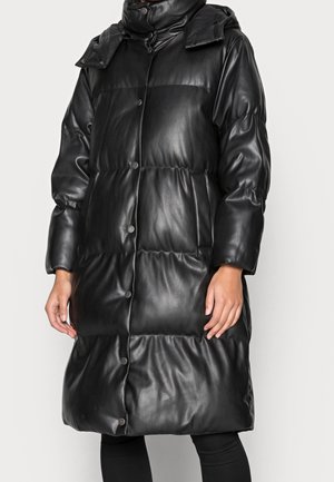 Manteau long noir matelassé avec boutons-pression, col montant et poches latérales, porté par une personne sur un fond uni.