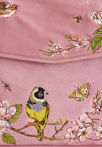 Un tejido de color rosa texturizado presenta un intrincado bordado de un pájaro amarillo sobre una rama, rodeado de flores, abejas y mariposas en colores vibrantes.