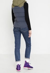 Puffvest i mörkgrått med olivgrön huva, svart långärmad tröja och blå jeans. Lila högtoppsskor med vita sulor.