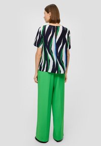 Blouse à manches courtes avec un motif ondulé noir, blanc et vert ; associée à un pantalon vert à jambes larges. Texture lisse et coupe décontractée.