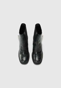 Juodi ankle batai su blizgiu gyvatės odos raštu, apvaliu nosiu, elastinėmis šoninėmis detalėmis ir plokščiu gumo padu. Dviejų atspalvių dizainas su matinėmis viršutinėmis dalimis.