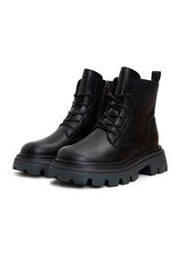 Paire de bottines à lacets en cuir noir avec semelles crantées épaisses et fermetures éclair latérales sur fond blanc.