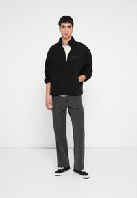 Μαύρο φλις πουλόβερ με φερμουάρ στον γιακά, συνδυασμένο με γκρι παντελόνι με κάθετες ρίγες και μαύρα αθλητικά παπούτσια. Απλός, καθημερινός σχεδιασμός με τσέπες.