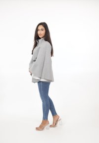 Capa estilo abrigo de mezcla de lana gris con cuello alto, combinada con jeans ajustados azul claro y sandalias de tacón transparente.