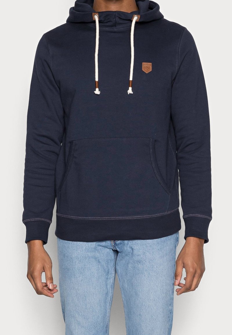 Námornicko modrá mikina s kapucí vyrobená z měkké bavlny, s klokaní kapsou, stahovacími šňůrkami, koženou nášivkou a žebrovanými manžetami a spodním lemem.