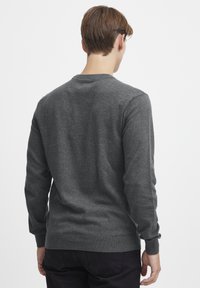 Suéter de punto gris con mangas largas y un escote redondo. Presenta puños y dobladillo acanalados, textura suave y una silueta ajustada.