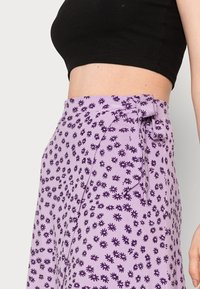 Saia envolvente roxa com um padrão floral em roxo escuro, detalhe de laço na cintura e uma textura de tecido leve e suave.