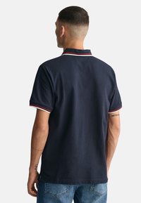 Polo azul marino con un acabado texturizado, que presenta una tapeta de tres botones, cuello y puños a rayas contrastantes en blanco y rojo, y mangas cortas.
