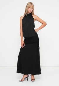 Vestido preto com design de halter, textura franzida e franzido lateral; emparelhado com sapatos de salto pretos e brancos com padrão.