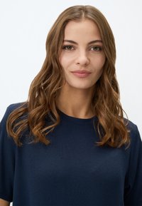 Top corto a maniche corte di colore blu navy a righe, con scollatura rotonda, caratterizzato da un tessuto texturizzato e una vestibilità rilassata. I capelli sono mossi e di lunghezza media.