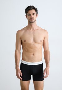 Boxeri negri cu talie elastică albă, având logo-ul Calvin Klein. Materialul pare neted și elastic.