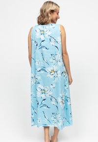 Maxi abito senza maniche blu chiaro con motivi floreali bianchi e gialli, tessuto fluido e silhouette rilassata.