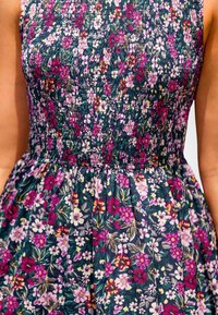 Vestido floral con una base azul oscura y un patrón colorido de flores moradas, rosas y blancas; cuerpo fruncido texturizado; falda acampanada.