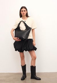 Svart läder tote-väska med en böjd form, slät textur och två axelremmar. Bärs med en krämfärgad topp och svart kjol.