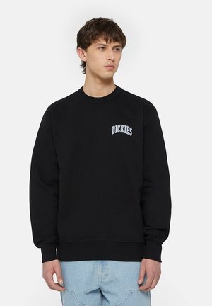 Mustat huppari, jossa on pyöreä kaula-aukko ja pitkät hihat. Vasemmassa rinnassa on sininen brodeerattu "DICKIES"-logo. Pehmeä kangas.