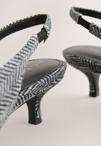 Juodo ir balto kvadratinio rašto aukštakulniai su tekstūriniu audinio viršumi, plonu vingiuotu kulnu ir juodu odiniu vidpadžiu.