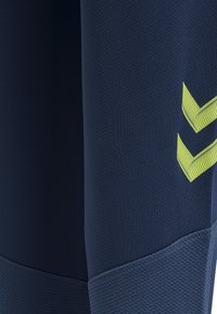 Marineblauwe atletische longsleeve top van een gestructureerde stof, met een opvallend geel chevrondetail op de bovenste mouw.