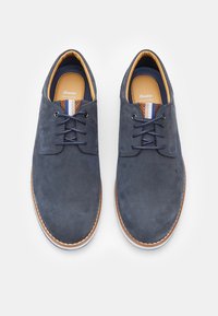 Navy blue suede shoes with a smooth texture, round toe, brown accents, and contrasting white and blue striped detail on top. Lace-up style.