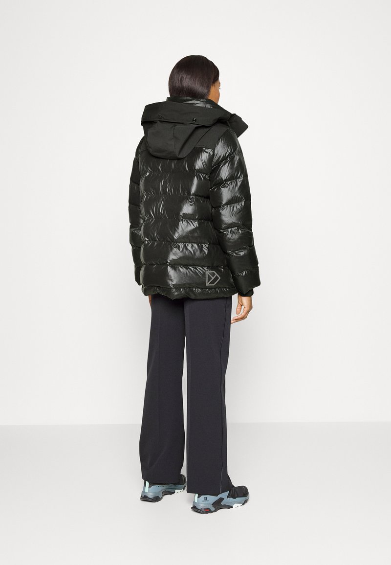 Schwarze Pufferjacke mit glänzender Textur, Kapuze und horizontalem Steppmuster. Kombiniert mit dunklen Hosen und Sportschuhen.