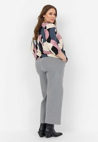 Top multicolore con forme astratte in rosa, nero e crema; pantaloni grigi; stivali a punta neri con tacco; texture del tessuto liscia.