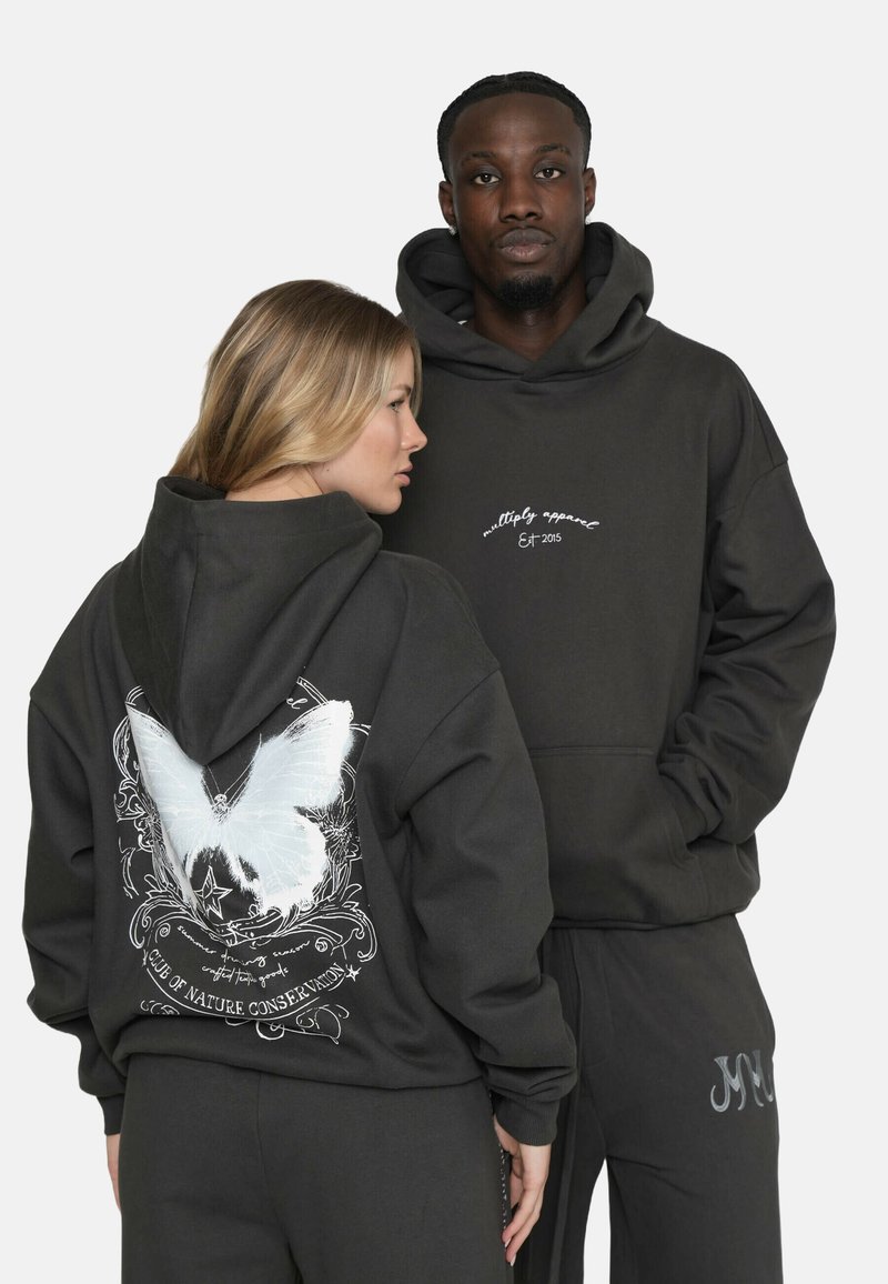 Dunkelgraue Hoodies zeigen ein großes weißes Schmetterlingsdesign auf dem Rücken und Text auf der Vorderseite. Das Model trägt passende Hosen mit einem Logopunkt.