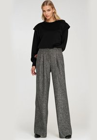 Czarny top z długim rękawem z falbanami na ramionach, w połączeniu z wysokimi spodniami o szerokich nogawkach z tweedu w szarym wzorze. Gładkie tekstury i dopasowany pas.