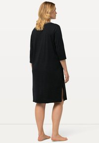 Schwarzes Kleid mit weißen Polka-Dots, 3/4-Ärmeln, seitlichen Schlitzen und einer lockeren Passform, gefertigt aus weichem Stoff. Besitzt einen runden Halsausschnitt.