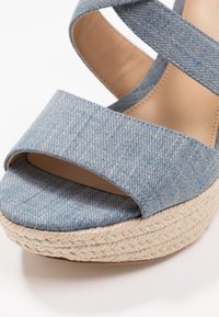 Sandały na platformie z denimu z szeroką, niebieską górą z tkaniny z krzyżującymi się paskami, podeszwą pokrytą płótnem oraz plecioną jucie w środkowej części.