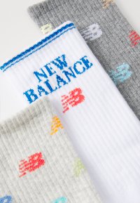 Tre par New Balance sokker: hvite med blå striper og logo, grå med fargerike detaljer, og lys grå med oransje og grønne mønstre.