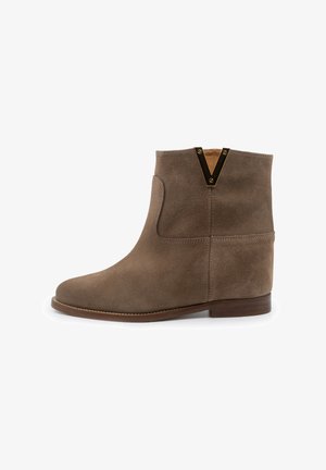 Bottine en daim brun avec un petit talon en bois et un accent en métal noir en forme de V sur le bord supérieur.