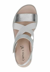 Stříbrné kovové kožené sandály na pásku s křížovými elastickými pásky, měkkou béžovou stélkou a texturovanou podrážkou. Viditelné logo značky "Caprice".