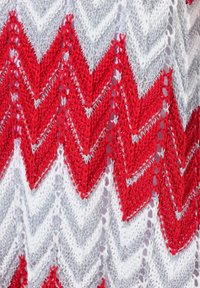 Tessuto lavorato a maglia con motivo a zigzag in rosso, argento e bianco, con una finitura testurizzata, caratterizzato da un mix di punti solidi e punti aperti.
