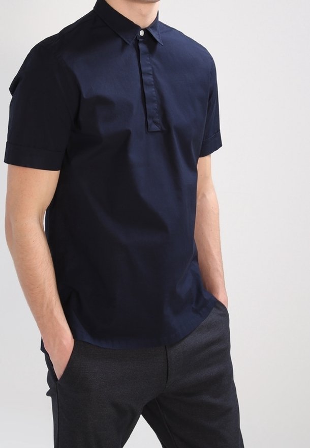 Polo-shirt à manches courtes navy avec patte de boutonnage et poignets rabattus. Le tissu a une texture lisse et une silhouette ajustée.