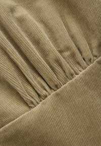 Tessuto in corduroy di un verde oliva attenuato, con righe verticali e dettagli arricciati lungo le cuciture, creando una superficie testurizzata.