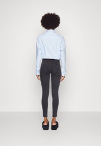 Jeans pitillo negros de cintura alta, tela suave y dos bolsillos traseros, combinados con una camisa de manga larga azul claro y sandalias negras de plataforma.