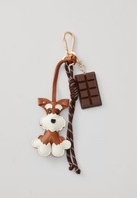Pendentif en cuir d'un chien brun et blanc avec des yeux noirs. Porte-clés en forme de barre chocolatée. Corde brune avec des rayures blanches. Clip en métal or.