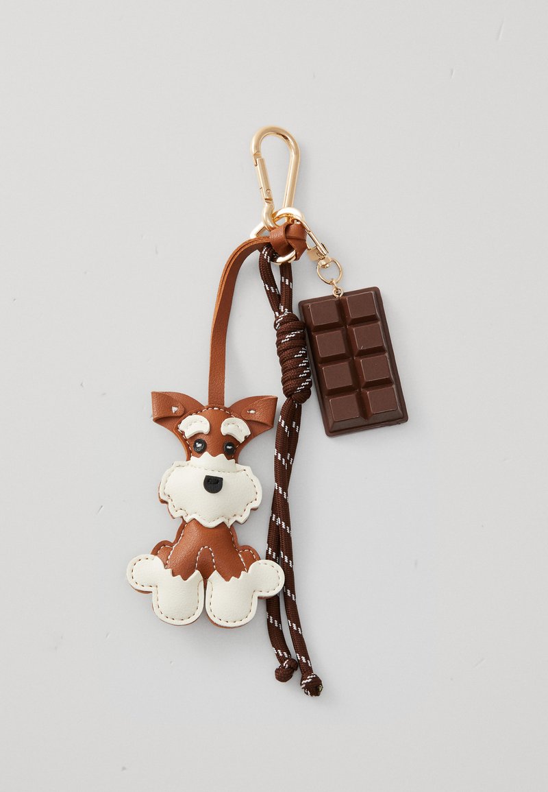 Pendentif en cuir d'un chien brun et blanc avec des yeux noirs. Porte-clés en forme de barre chocolatée. Corde brune avec des rayures blanches. Clip en métal or.