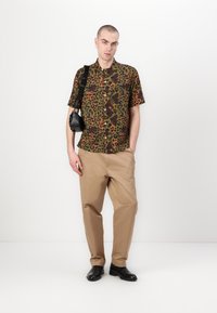 Camisa de leopardo de manga corta en verde, naranja y negro, combinada con chinos color crema y botas negras de tobillo. Pequeño bolso de hombro con detalles metálicos.