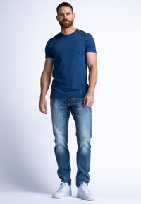 Granatowa koszulka typu crew neck, krótki rękaw, slim fit. W zestawie z jasnoniebieskimi, postrzępionymi dżinsami i białymi sneakersami. Dostosowany projekt dla lepszej czytelności.