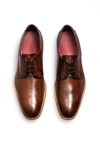 Paar polierte braune Lederschuhe mit Schnürsenkeln und hellen Holzsohlen, von oben auf weißem Hintergrund gezeigt.