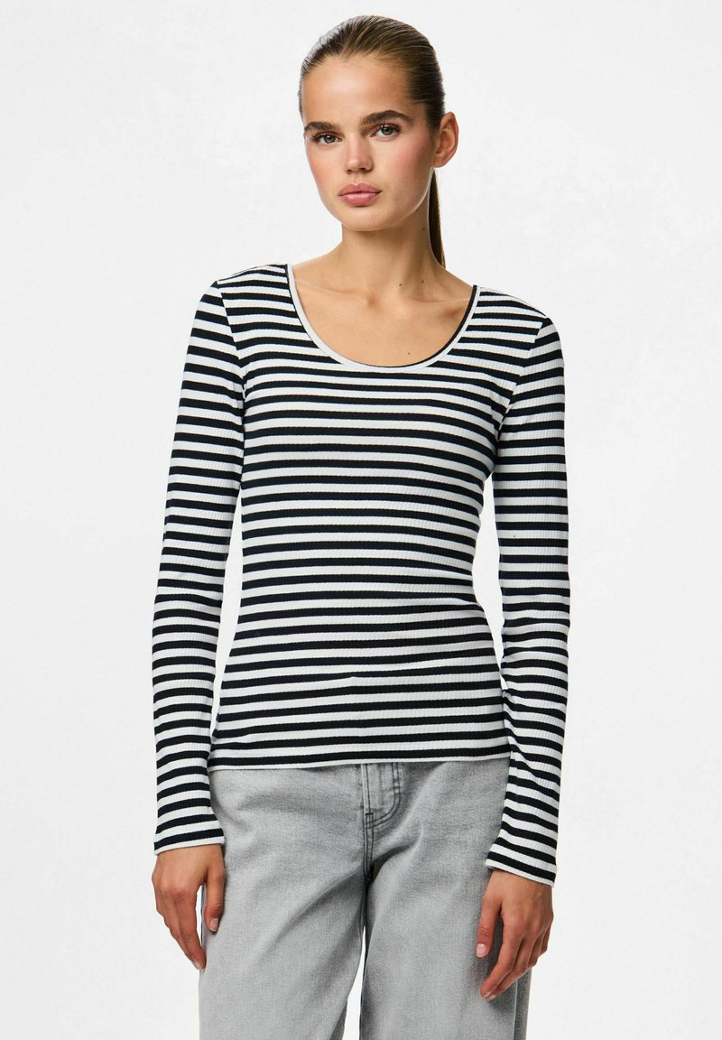 Černo-bílý pruhovaný dlouhý rukáv top s výstřihem do kulata, žebrovanou texturou a přiléhavým střihem. Nošený s světle šedými džíny.