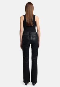 Czarne skórzane spodnie w stylu dzwonów o gładkiej teksturze, z średnim stanem i dwiema tylnymi kieszeniami, zestawione z dopasowanym topem na ramiączkach.