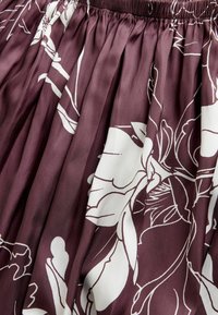 Bordowa plisowana spódnica wykonana z gładkiej tkaniny, zdobiona dużymi białymi wzorami kwiatowymi i elastycznym pasem dla wygody.
