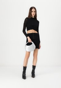 Čierny dlhý rukáv crop top s uzlom, skombinovaný s čiernou minisukňou s predným zipsom a striebornou kabelkou typu hobo. Čierne členkové topánky.